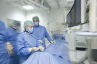 Ärzte im OP mit blauen Kitteln tragen grüne Hauben und weißen Mundschutz stehen vor Patienten, abgedeckt mit blauen Tüchern