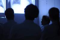 Abgedunkelter Raum, Ärzte folgen einem Vortrag mit Bildpräsentation an der Leinwand.