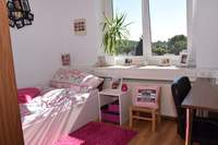 Zimmer im Personalwohnheim Blick zum Fenster, links Bett mit Nachttisch vor Fenster, rechts Schreibtisch, Dekoration in Pink