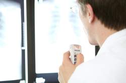 Ein Arzt blickt auf zwei Monitore und diktiert in ein Diktiergerät