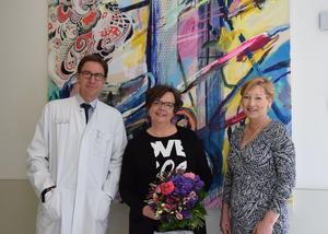 Prof. Dr. Bremer, Frau Falke und Frau Eschkötter stehen vor einem farbenfrohen abstrakten Gemälde